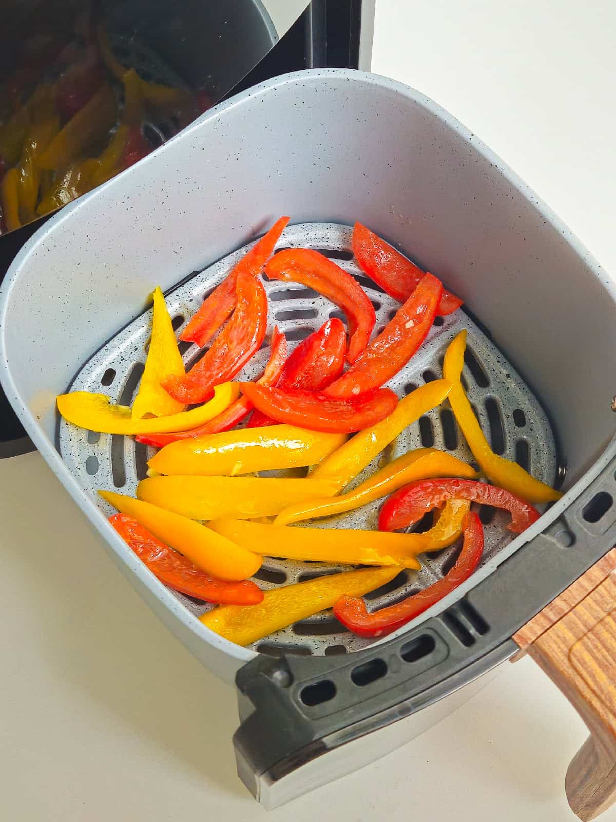 Seasoned bell peppers arranged in an air fryer basket before cooking.