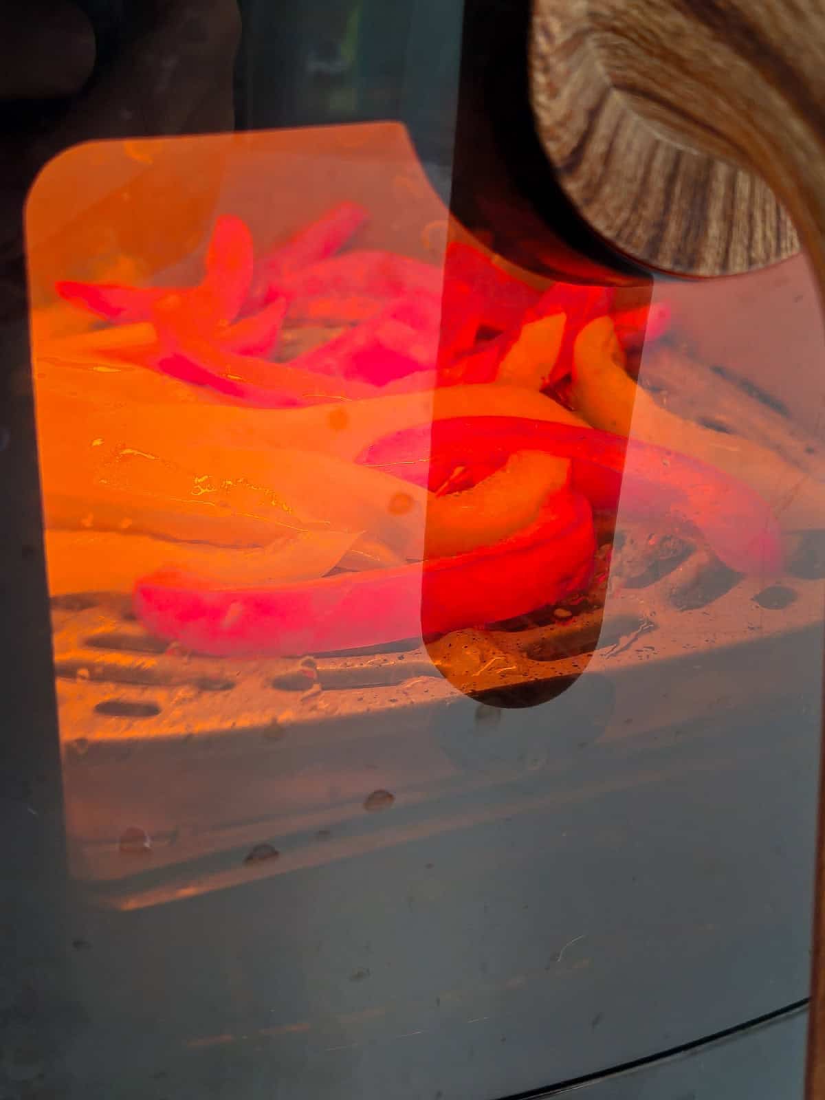 Red and yellow bell peppers roasting inside an air fryer under heat.