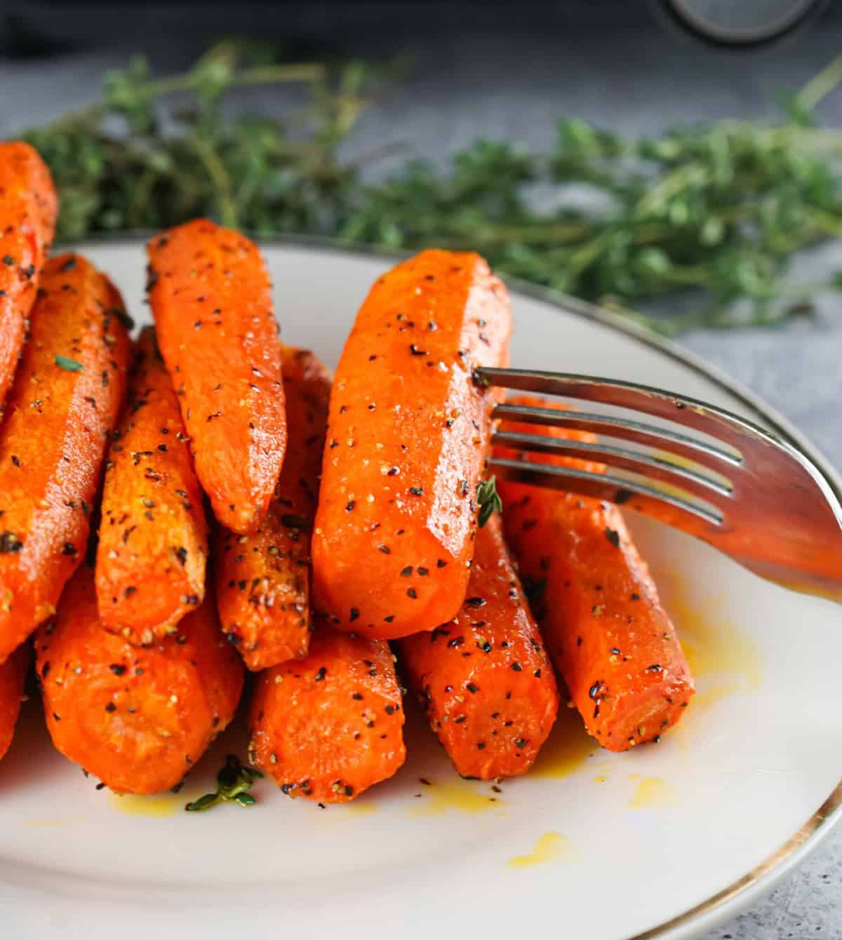 Tender air fryer roasted carrots seasoned with herbs and black pepper, served on a plate with a fork.