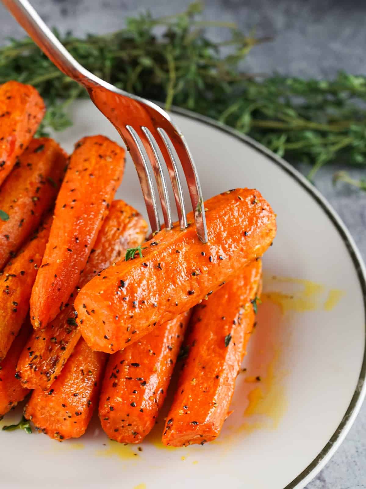 Juicy roasted air fryer carrots garnished with fresh herbs, ready to serve on a white plate with fork.