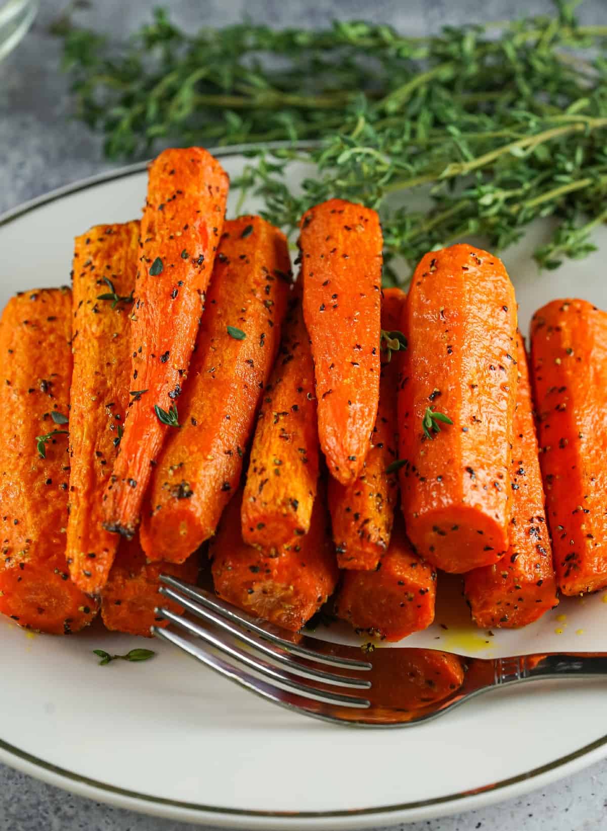 Plate of roasted air fryer carrots seasoned with herbs and black pepper, garnished with fresh thyme.