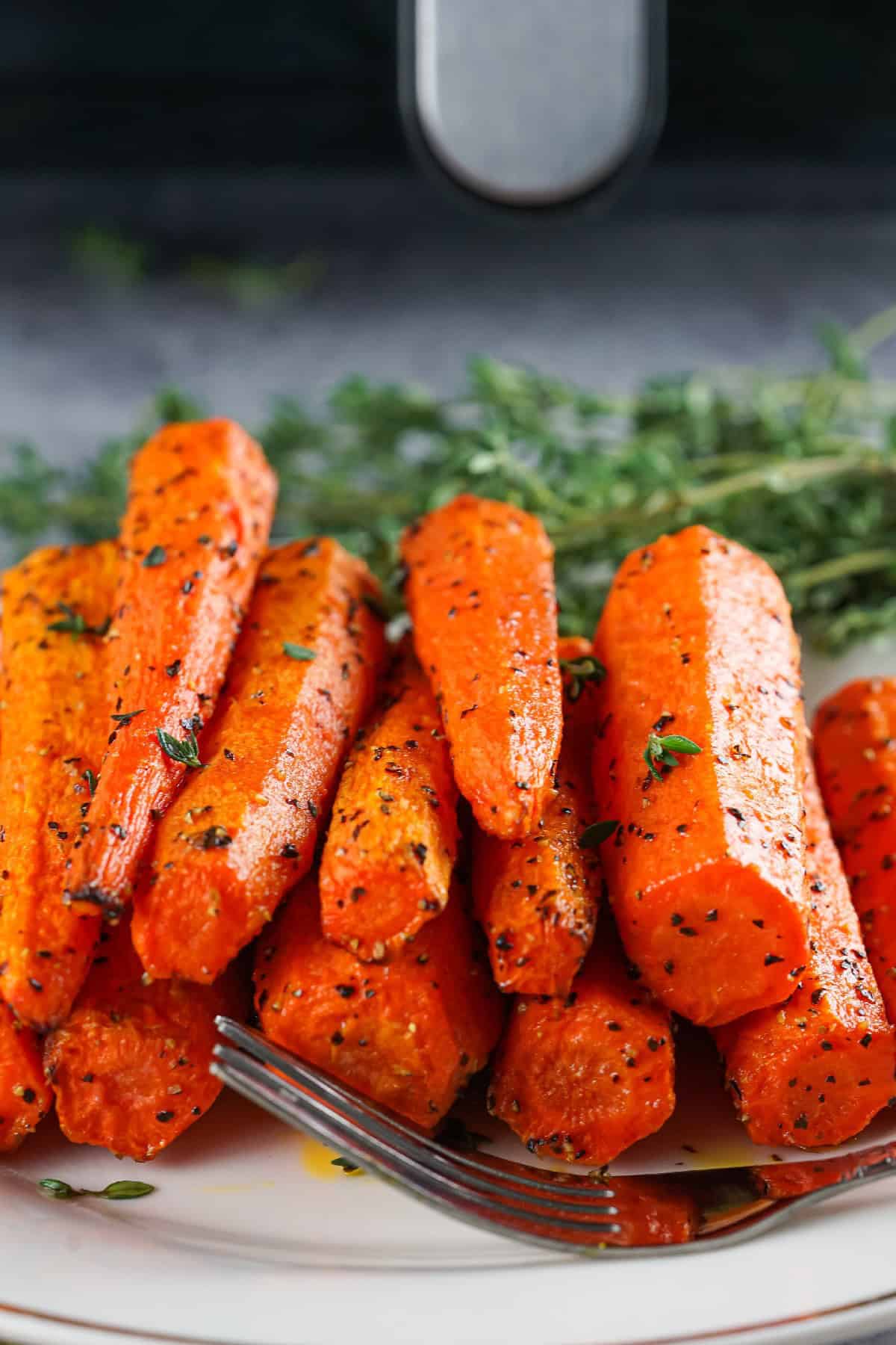 Close-up of crispy air fryer roasted carrots on a plate with fresh thyme garnish and black pepper seasoning.