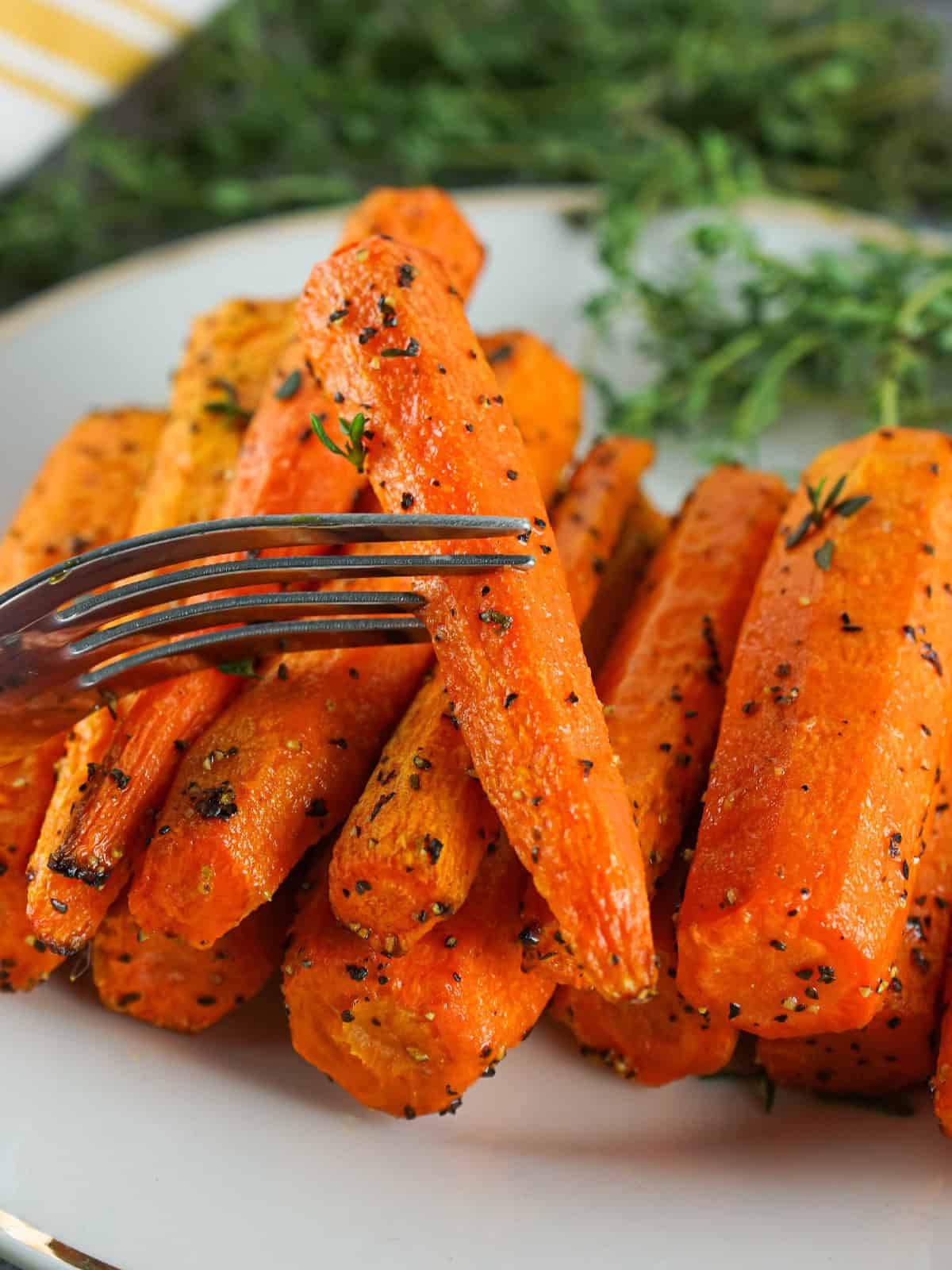 Fork lifting a roasted air fryer carrot from a plate of herb-seasoned carrots with fresh thyme garnish.