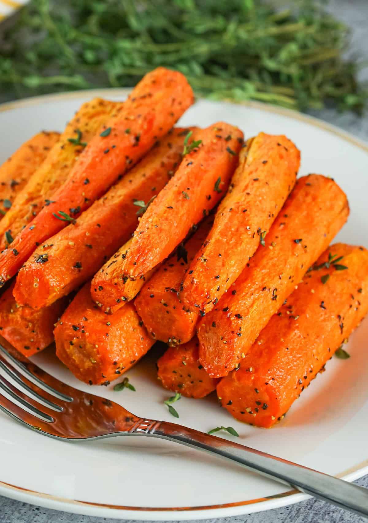Plate of golden roasted air fryer carrots sprinkled with fresh herbs and black pepper, ready to serve.