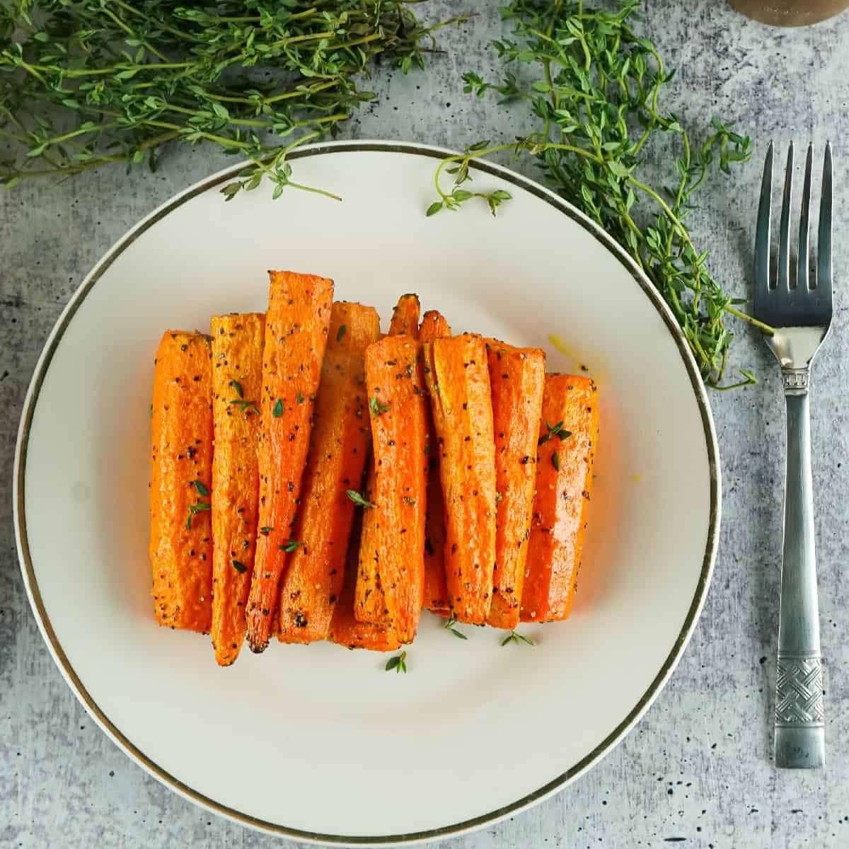 Overhead view of roasted air fryer carrots on a white plate, garnished with fresh thyme and black pepper.
