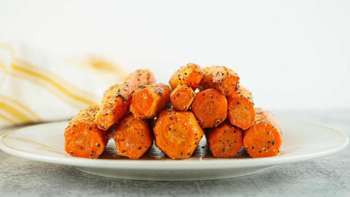 Stack of roasted air fryer carrots seasoned with herbs and black pepper, served on a white plate.