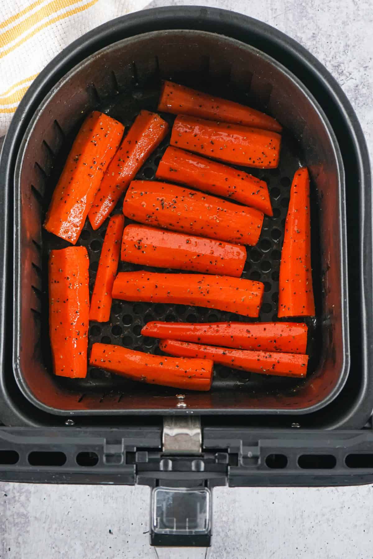 Seasoned carrot sticks arranged in an air fryer basket, ready for roasting into crispy air fryer carrots.