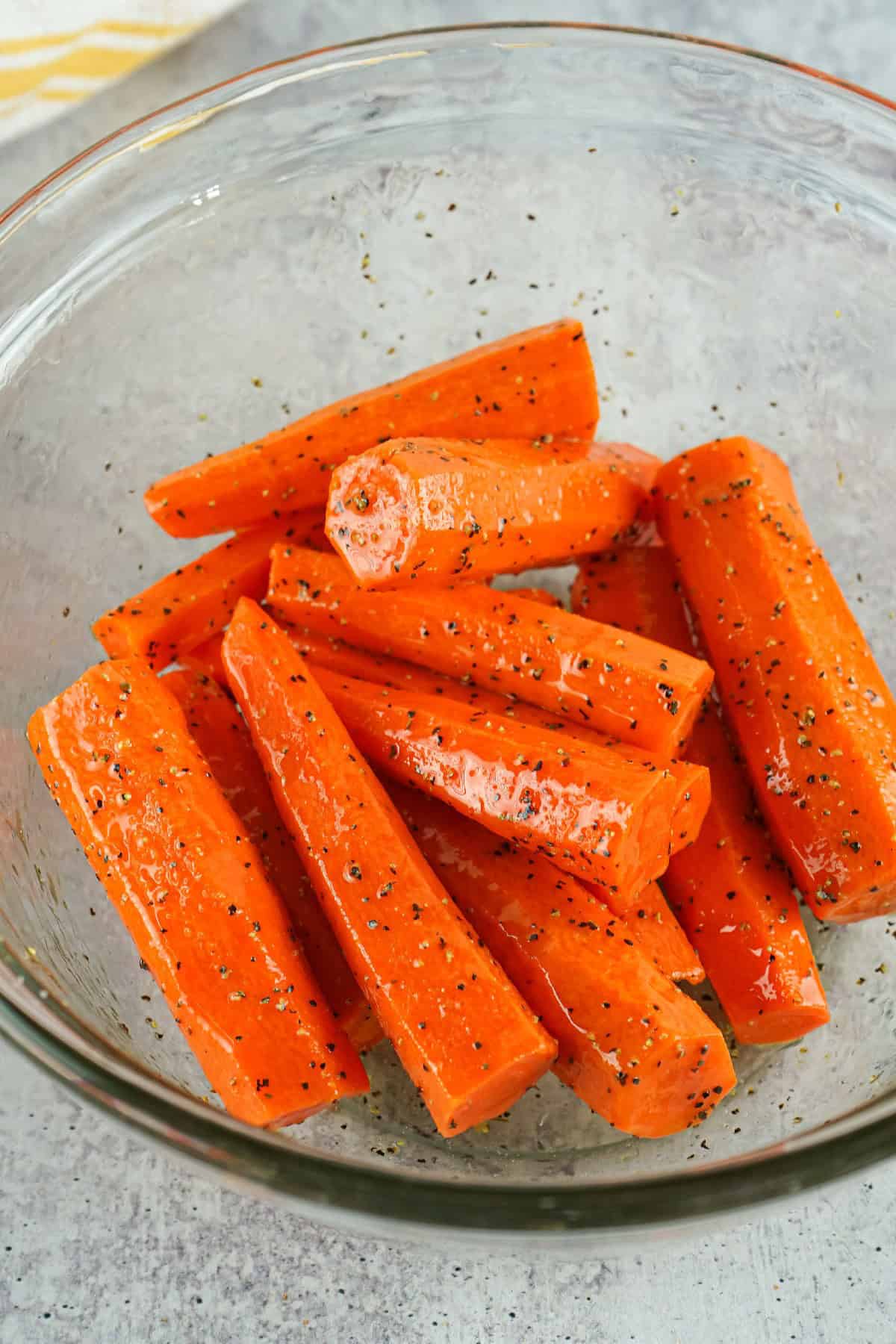 Fresh carrot sticks tossed with olive oil, salt, and pepper in a glass bowl for air fryer roasting.
