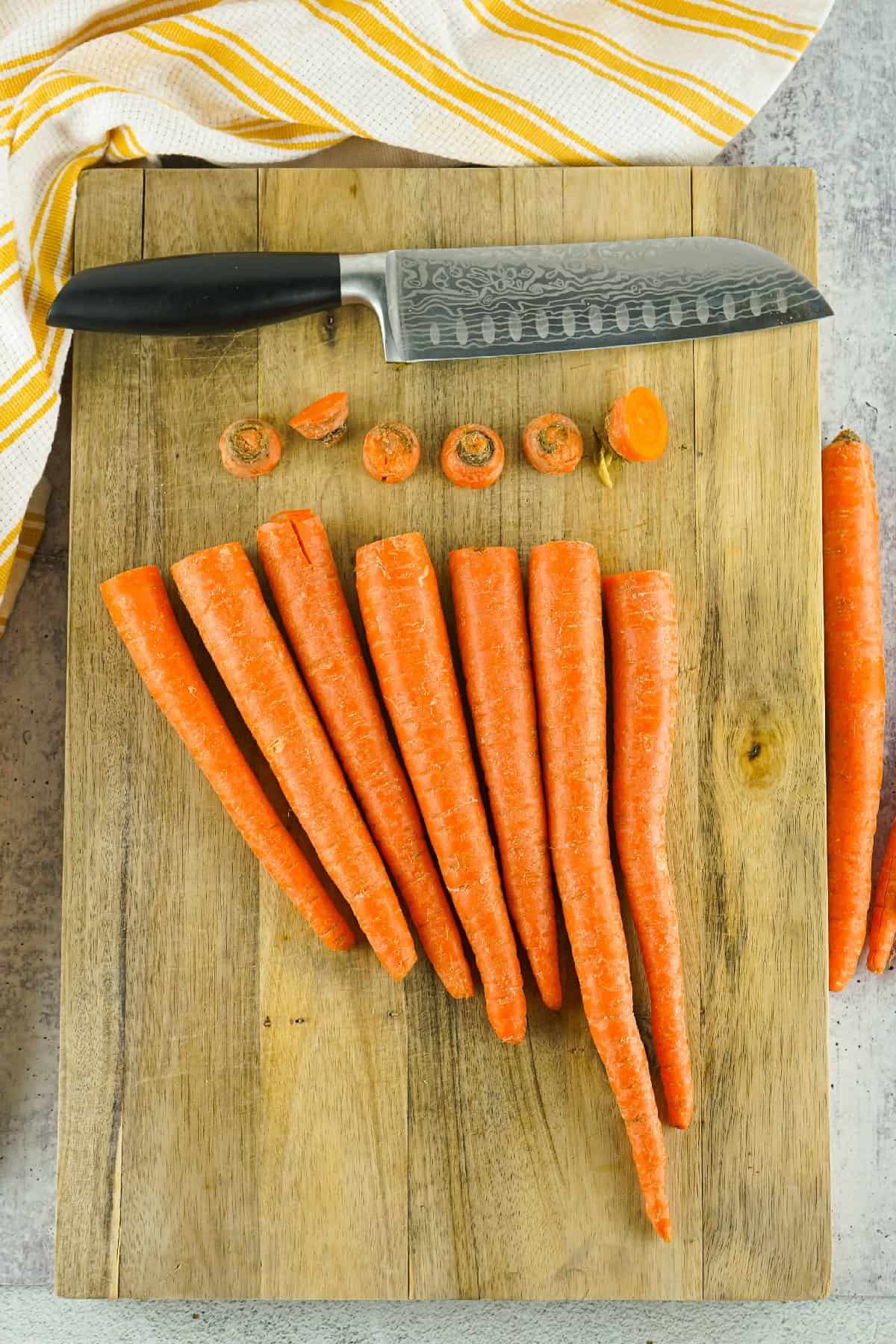 Fresh whole carrots on a wooden cutting board with knife, ready for air fryer recipe preparation.