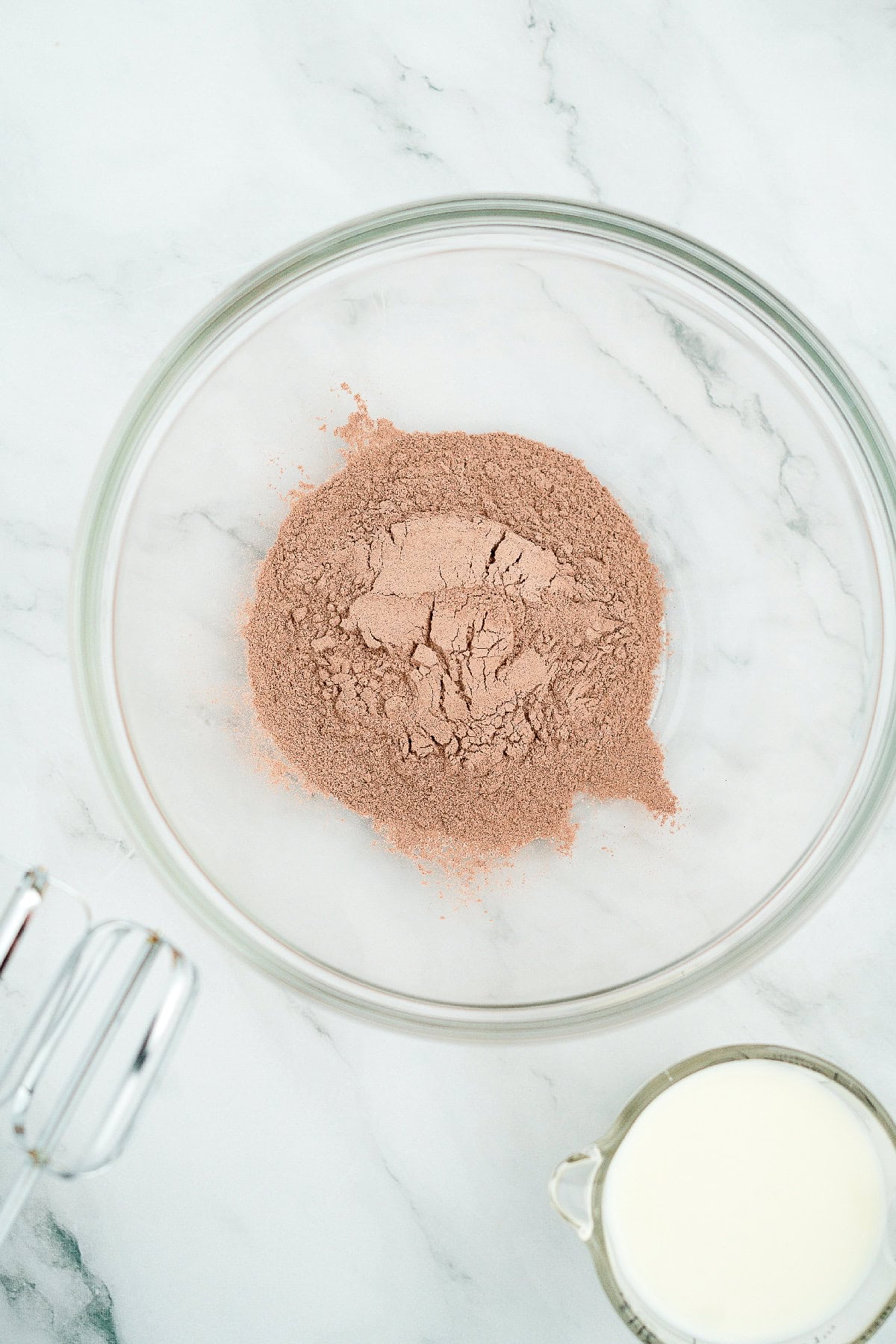 Clear glass bowl with instant chocolate pudding mix powder on a marble surface.