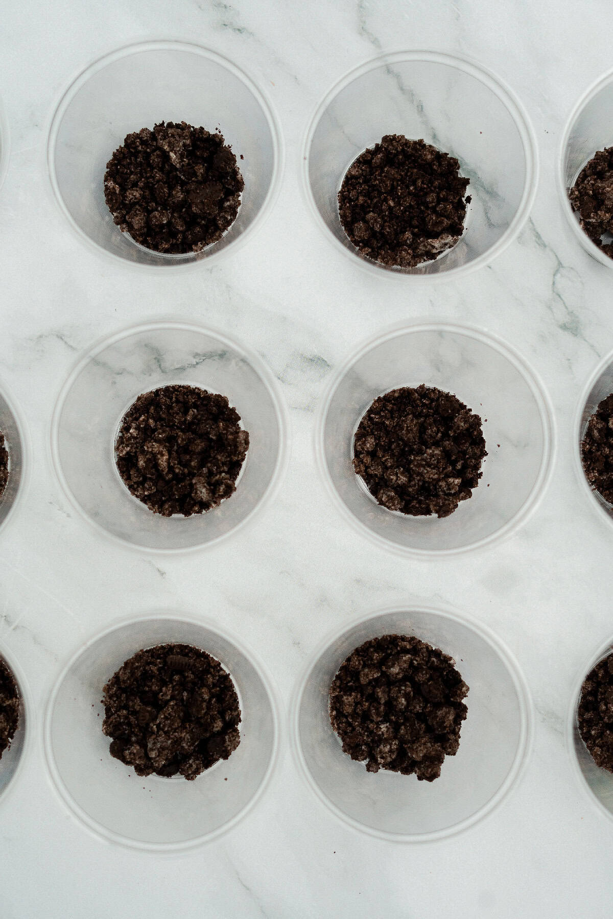 Clear plastic cups filled with a bottom layer of crushed Oreo cookie crumbs for Halloween dirt cake cups.