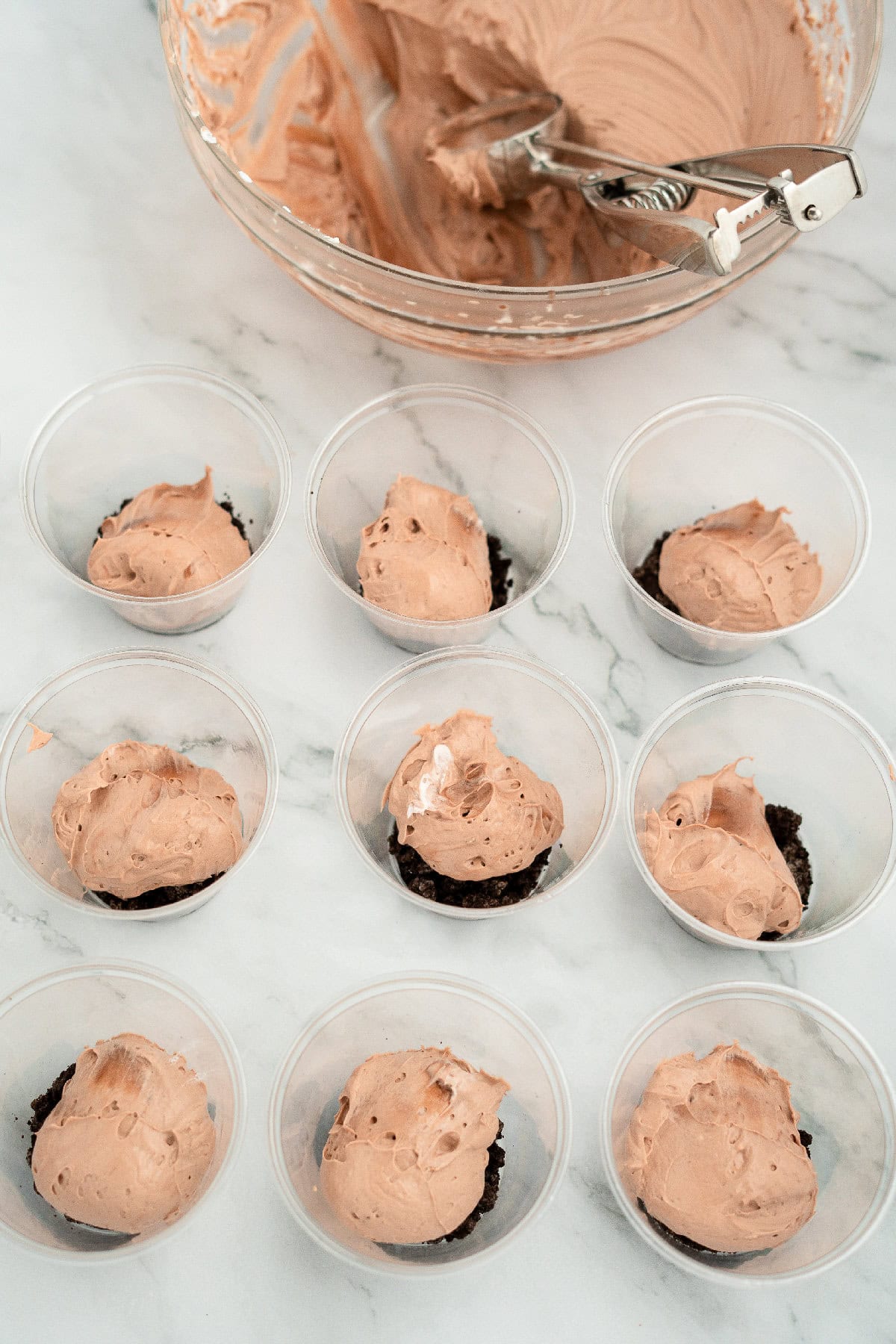 Plastic dessert cups with Oreo crumb base topped with scoops of chocolate pudding and cream cheese mixture.