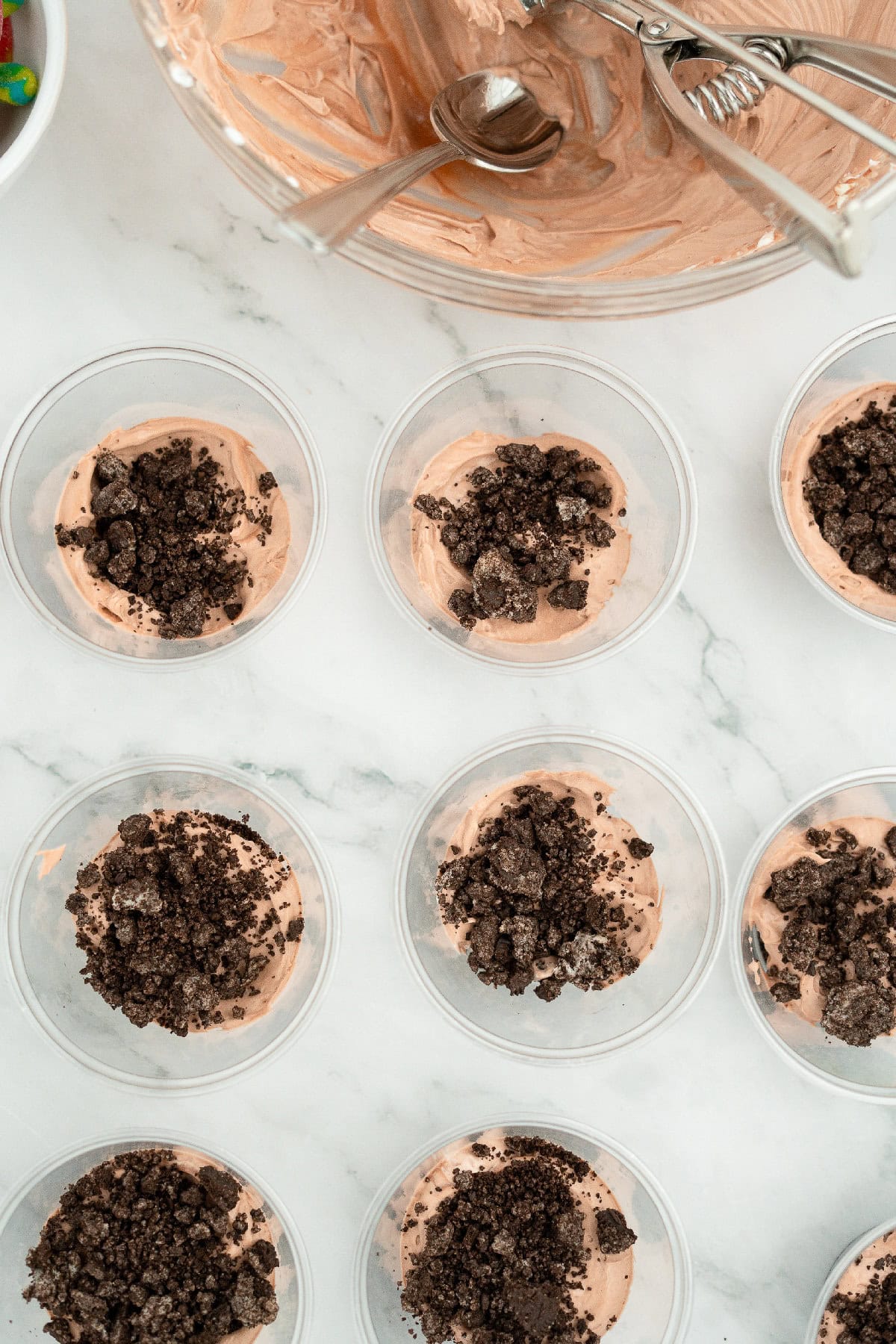 Dirt pudding cups layered with chocolate filling and topped with crushed Oreo cookie crumbs, ready for Halloween dessert assembly.