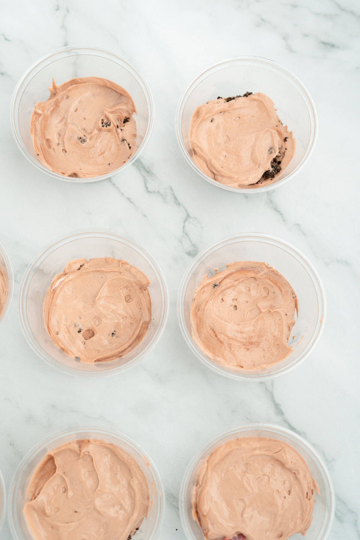 Dirt cake cups layered with creamy chocolate pudding mixture spread smoothly in clear plastic cups.