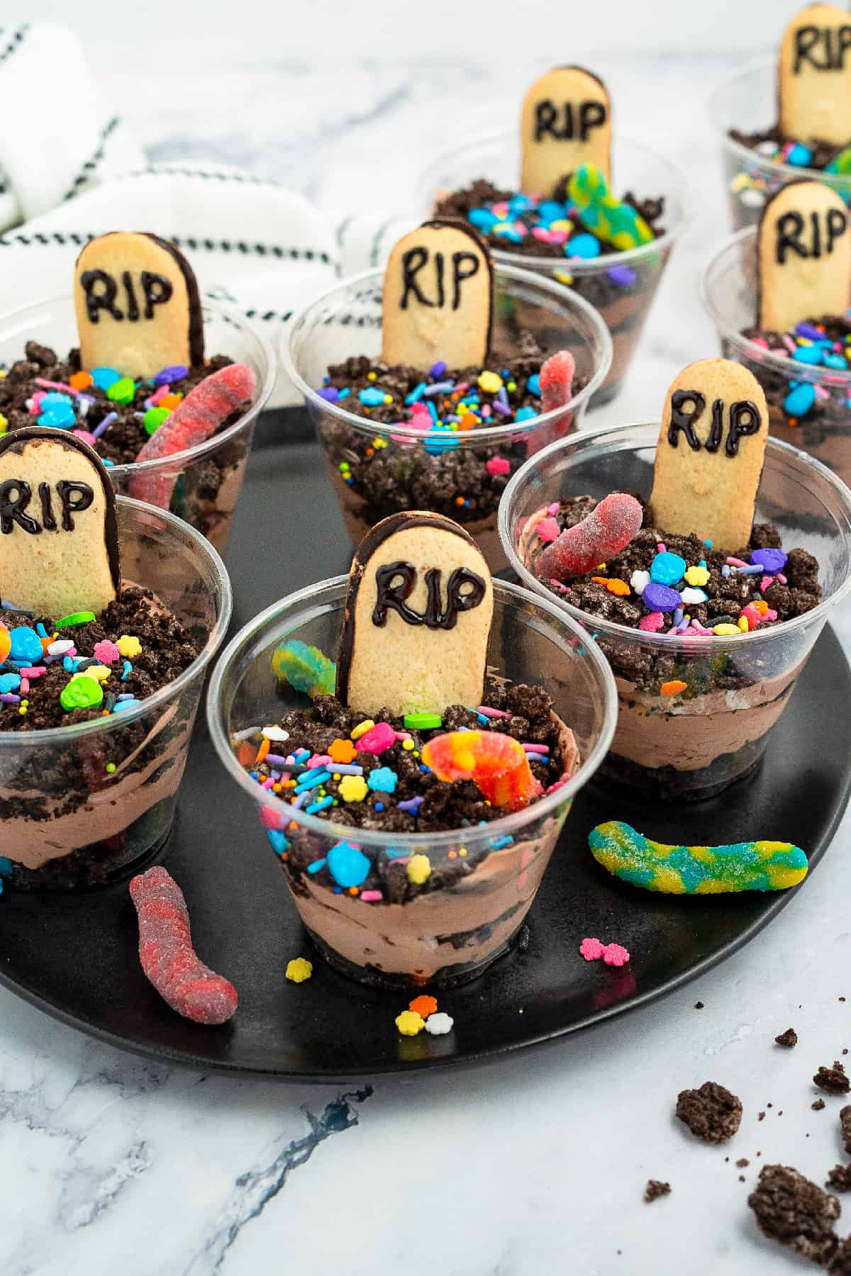 Individual Halloween dirt cake cup with Oreo crumbs, gummy worm candy, colorful sprinkles, and a RIP Milano cookie tombstone.