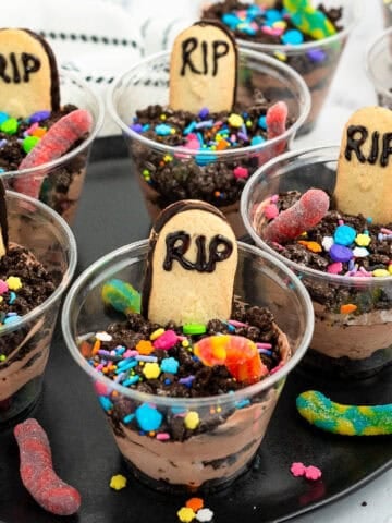 Spooky graveyard dirt pudding cups decorated with cookie tombstones, gummy worms, and bright Halloween sprinkles.