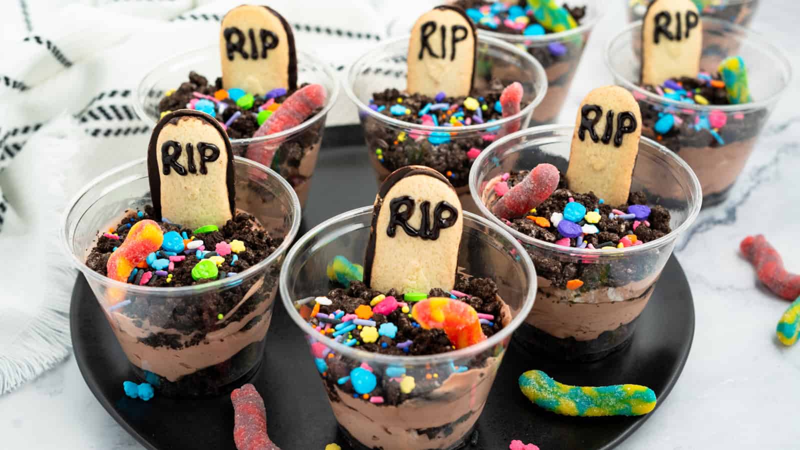Halloween dirt cake cups with RIP cookie gravestones, gummy worms, and festive sprinkles.