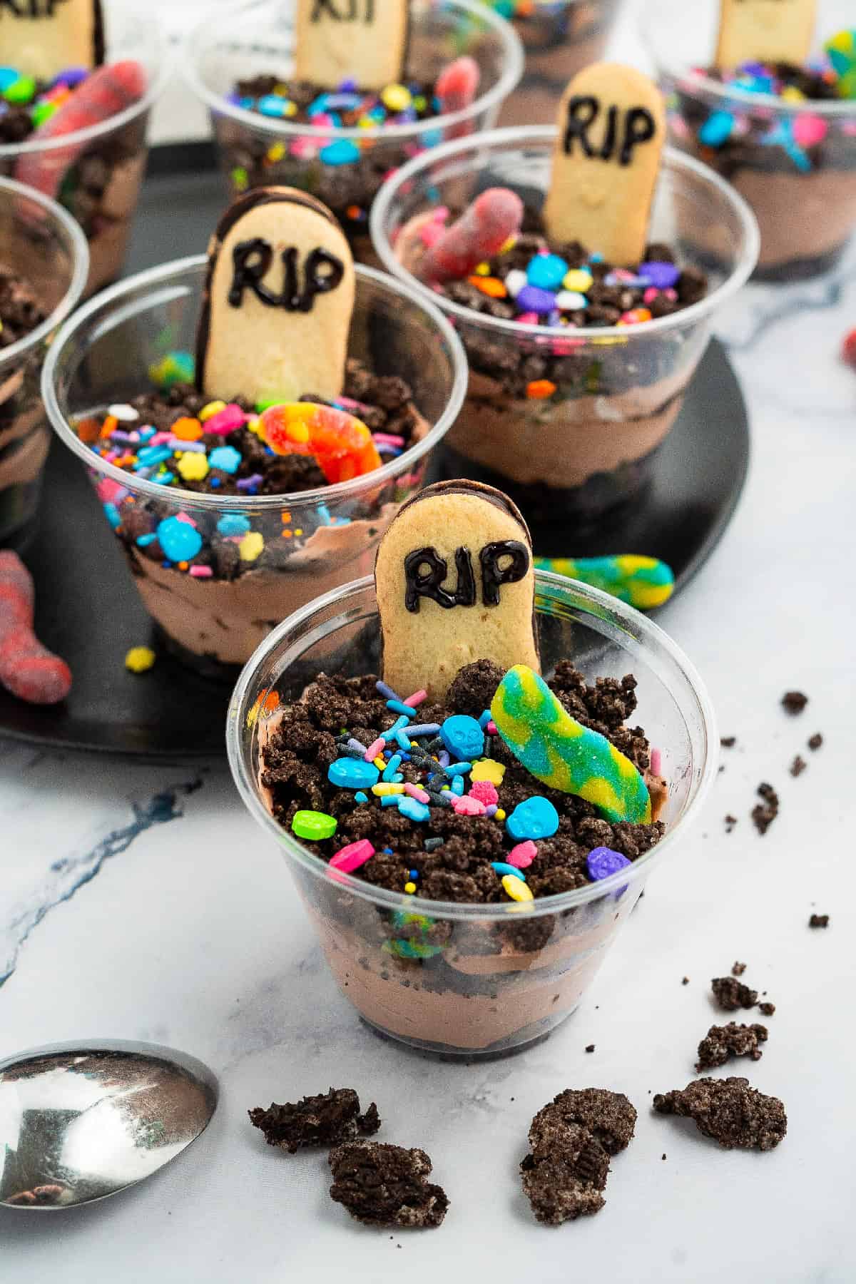 Festive no-bake Halloween dessert cups with Oreo crumbs, gummy worms, sprinkles, and RIP Milano cookies.