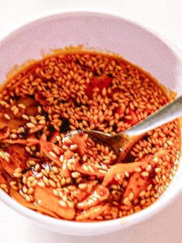 Homemade garlic chili oil with sesame seeds and fried garlic slices in a white bowl.
