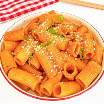 Bowl of gochujang pasta with spicy sauce, grated cheese, and green onions.