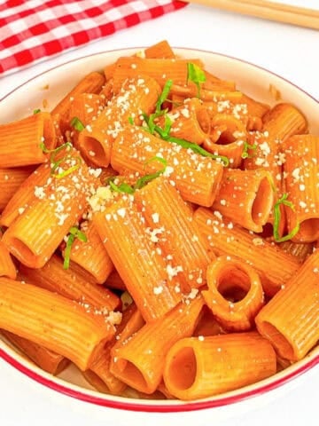 Bowl of gochujang pasta with spicy sauce, grated cheese, and green onions.