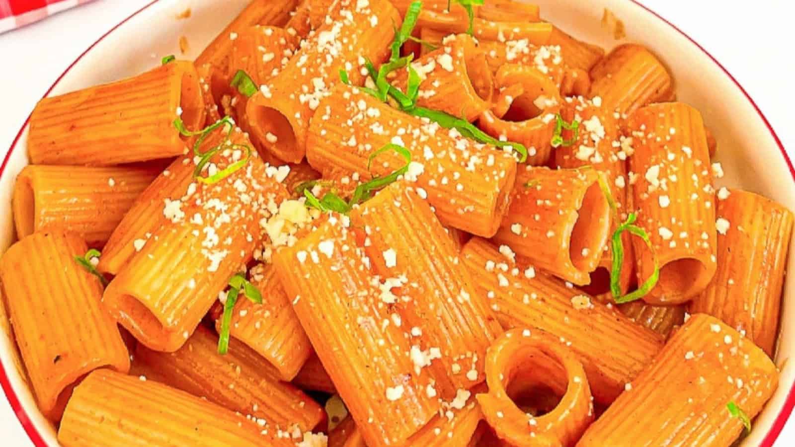 Spicy Korean gochujang pasta in a white bowl with scallions and cheese.
