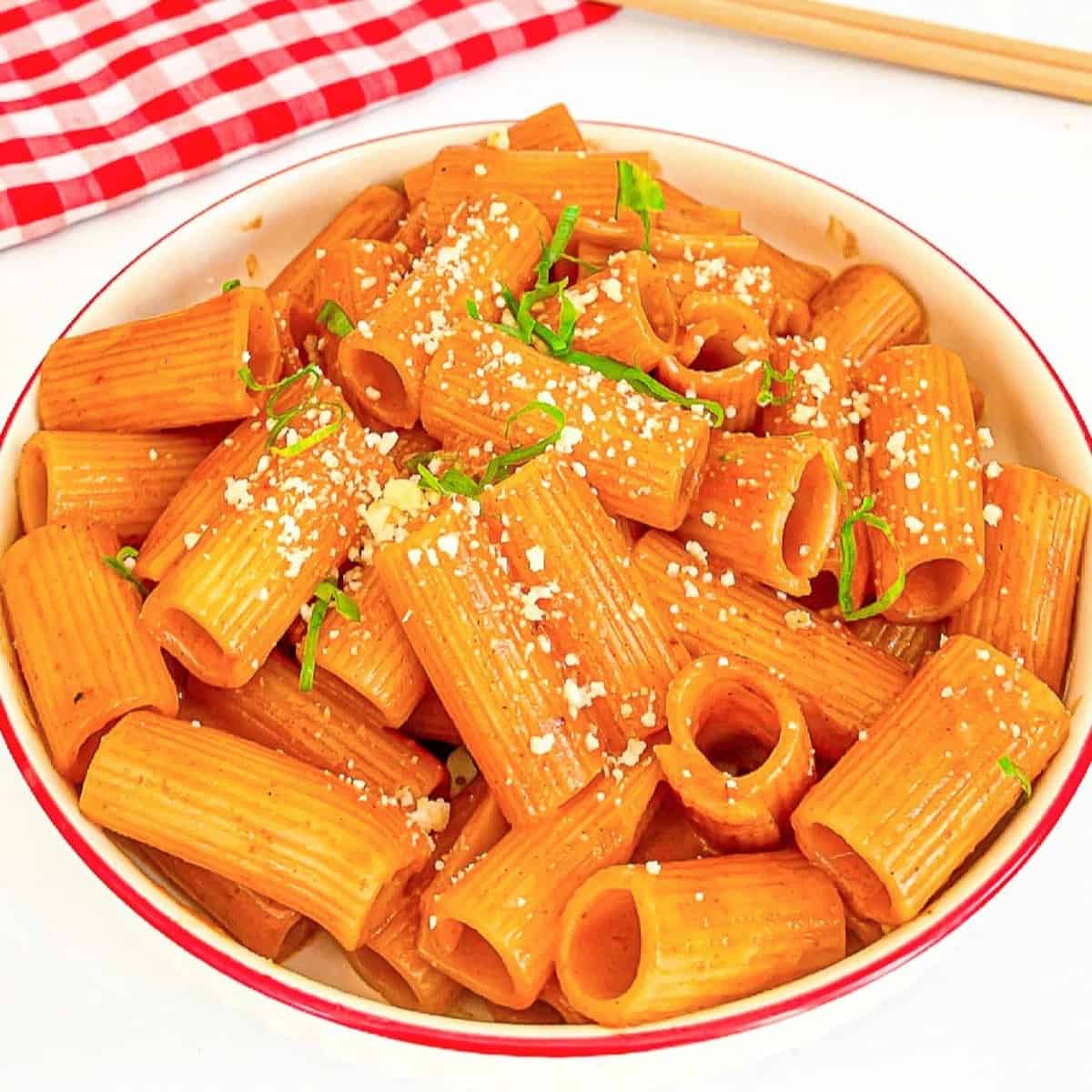 Bowl of gochujang pasta with spicy sauce, grated cheese, and green onions.