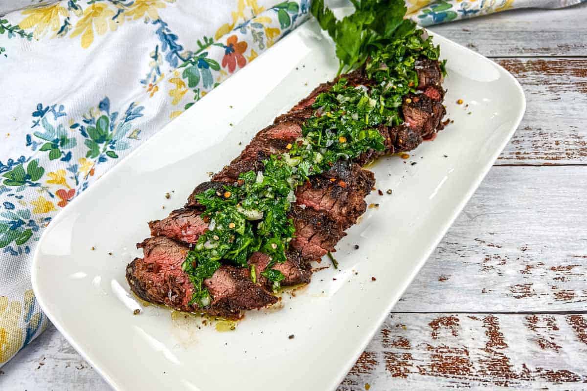 Sliced Grilled Hanger Steak with Chimichurri on a white plate.