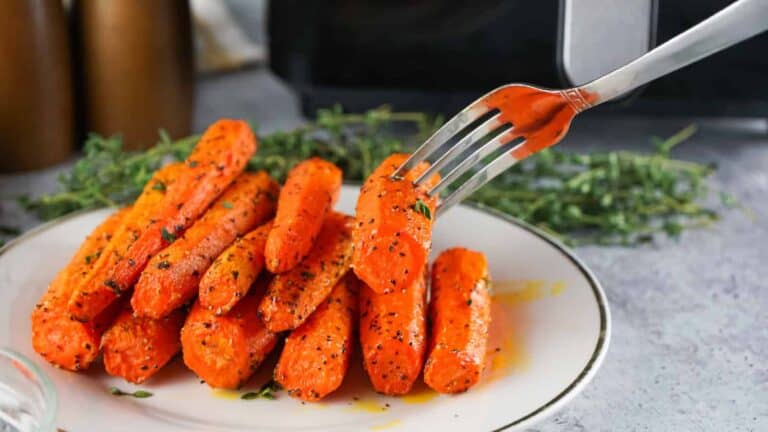 Fork lifting a roasted air fryer carrot from a plate of herb-seasoned carrots.