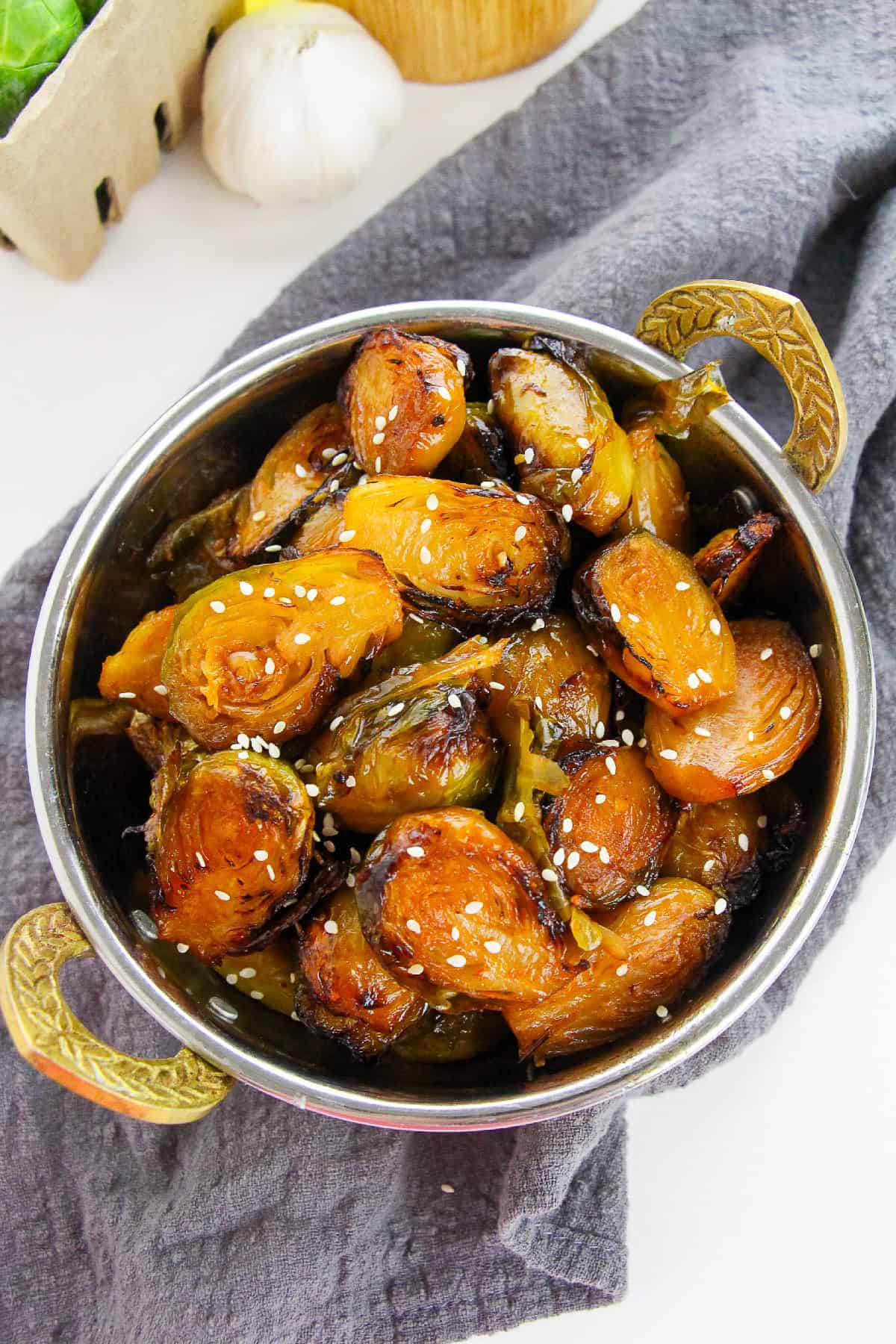 Sweet and spicy Korean Brussels sprouts served in a round copper bowl, topped with sesame seeds.