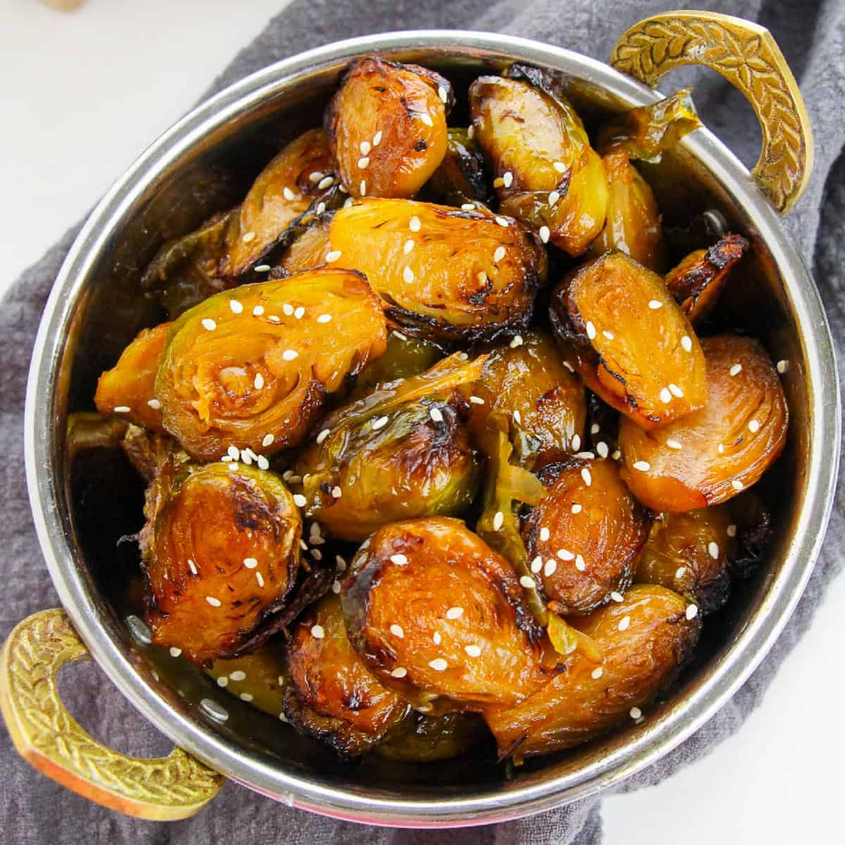Crispy air-fried Korean Brussels sprouts glazed with gochujang sauce and sprinkled with sesame seeds, served in a metal bowl.