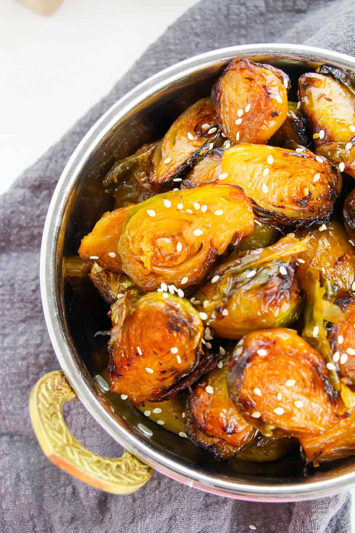Golden air-fried Brussels sprouts in a bowl with sesame seeds, highlighting crispy edges and glaze.