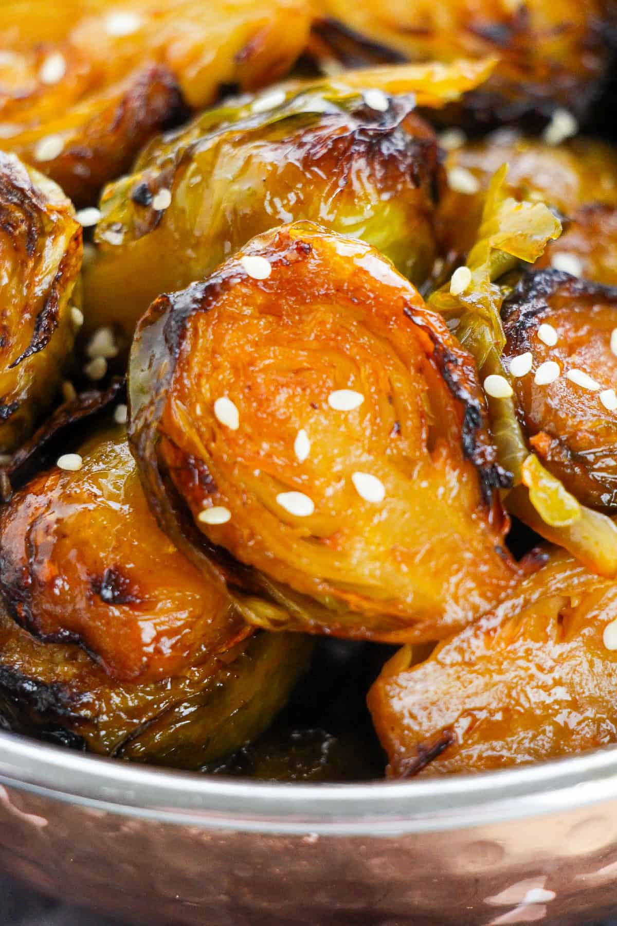 Close-up of glistening Brussels sprouts coated in gochujang glaze and sprinkled with sesame seeds.