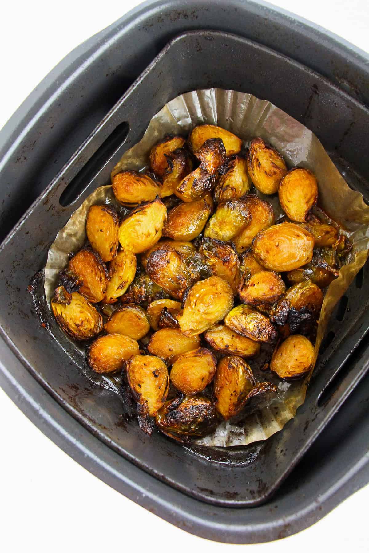 Crispy Korean Brussels sprouts air-fried to golden perfection in a parchment-lined air fryer basket.