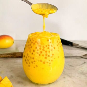A spoon dripping creamy mango sago pudding into a glass filled with tapioca pearls and rich mango coconut mixture.