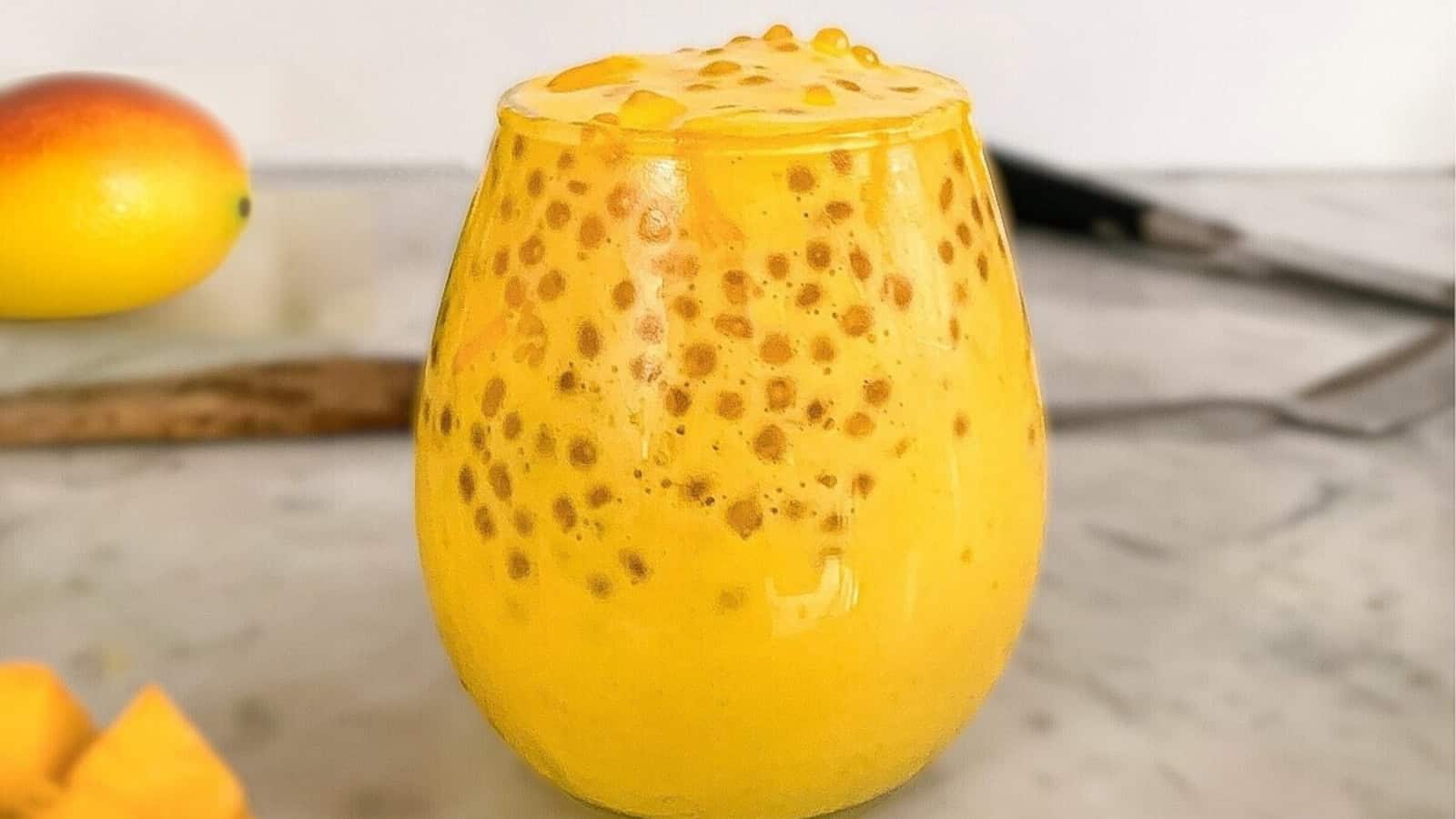 A glass of mango sago dessert topped with tapioca pearls, set on a marble countertop.