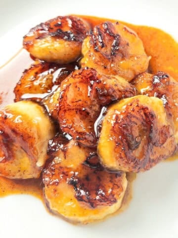 Caramelized pan fried bananas coated in a golden brown cinnamon sugar glaze served on a white plate.