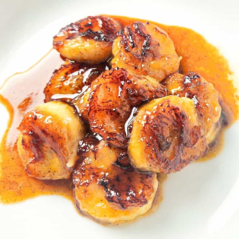 Caramelized pan fried bananas coated in a golden brown cinnamon sugar glaze served on a white plate.