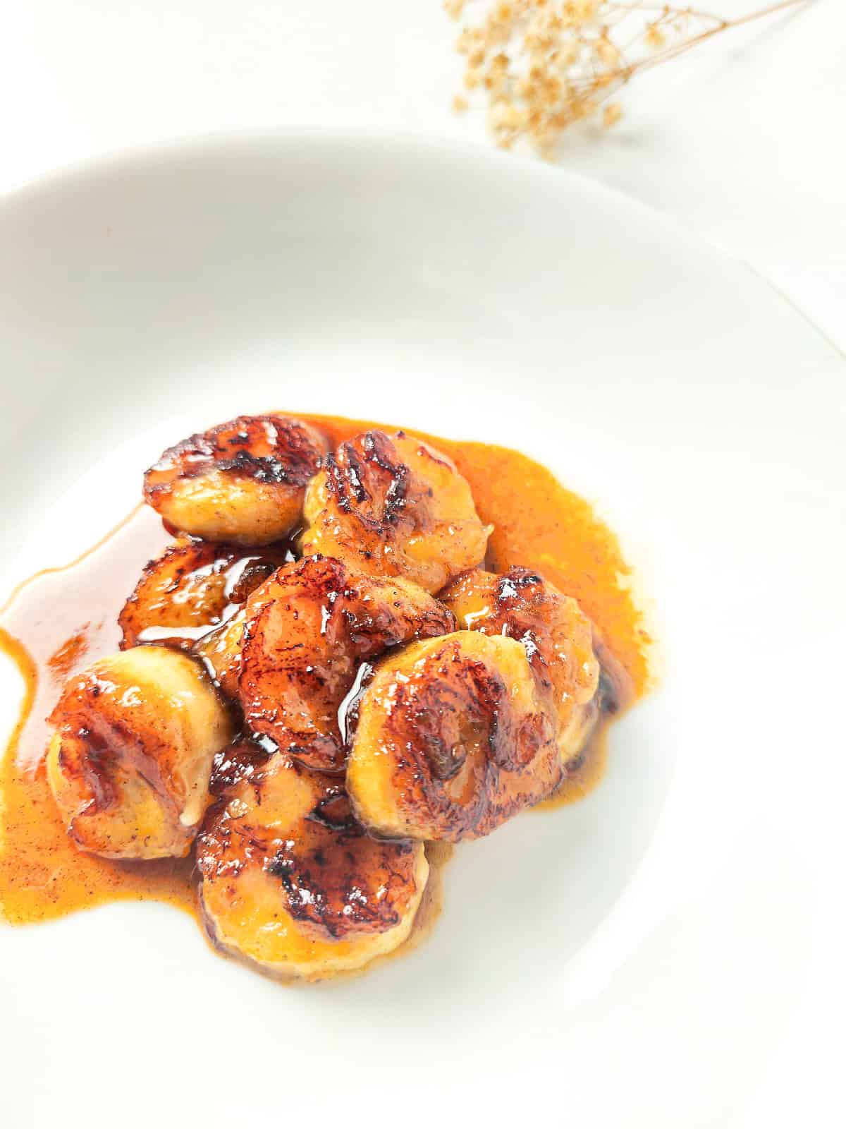 Pan fried bananas with caramelized edges and cinnamon glaze, styled on a white plate with a light background.