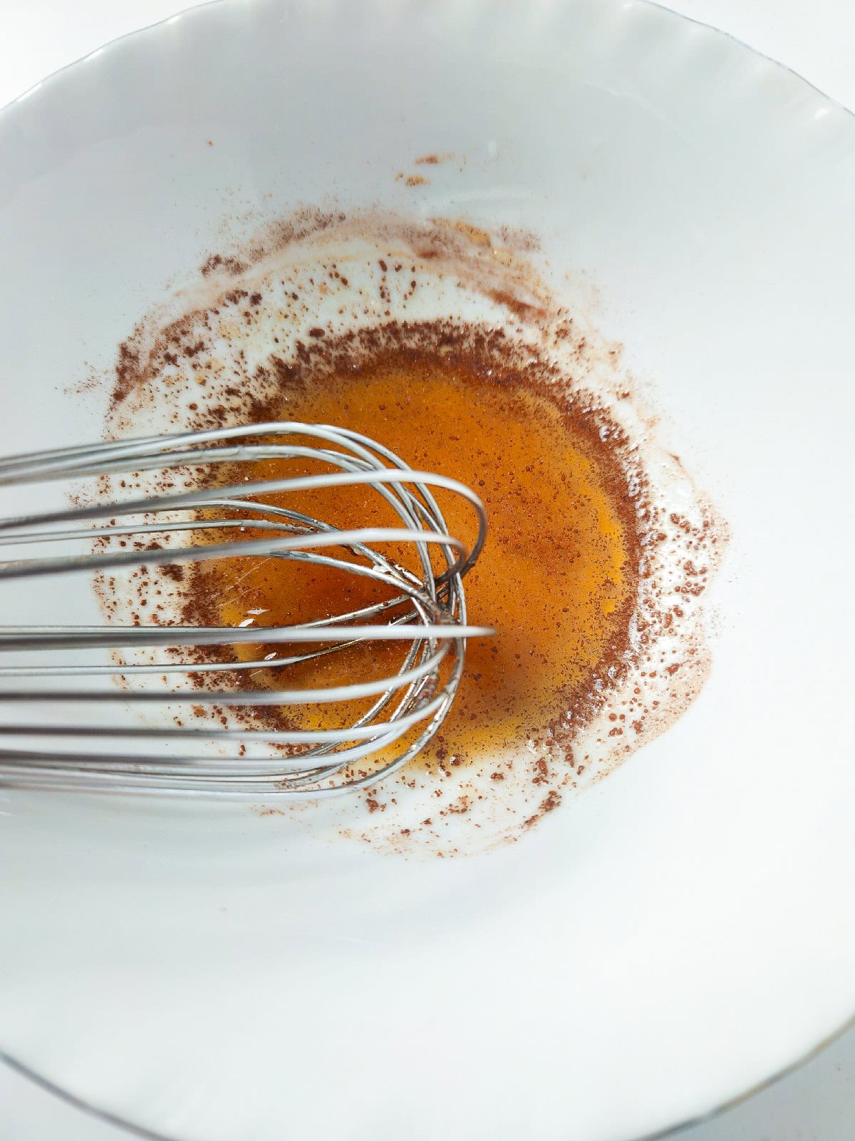 Whisk mixing honey, cinnamon, and vanilla in a white bowl to create glaze for fried bananas.