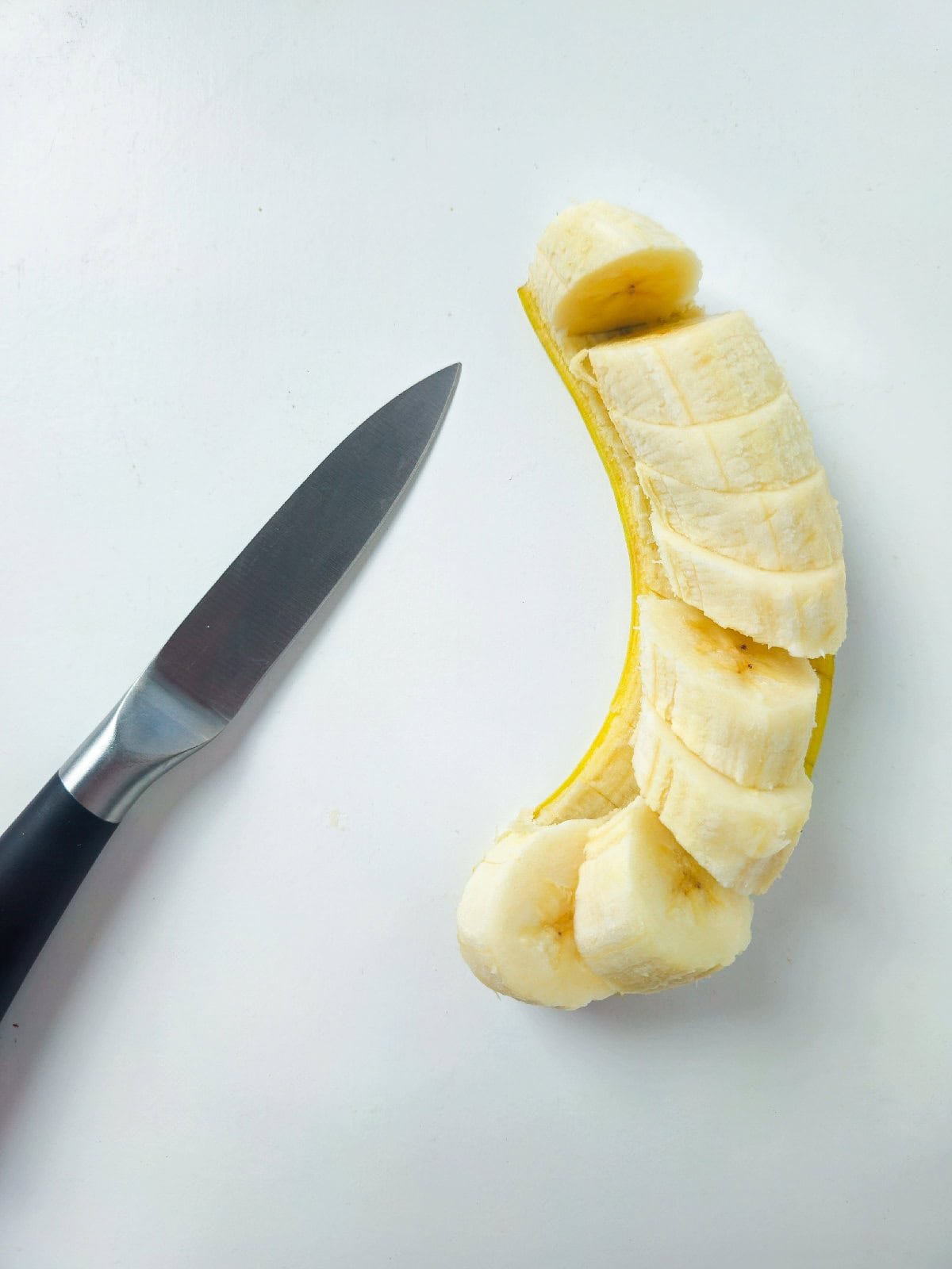 Fresh banana sliced into rounds with a knife, ready for pan frying.