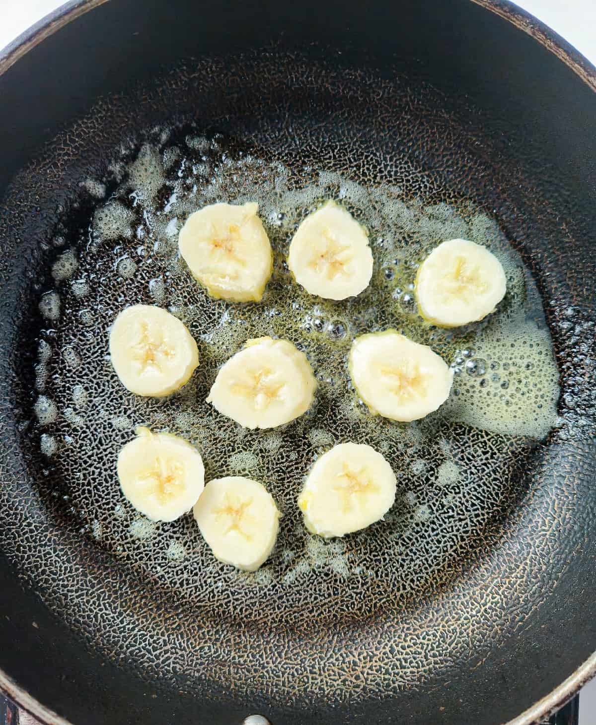 Sliced bananas cooking in melted butter inside a frying pan.