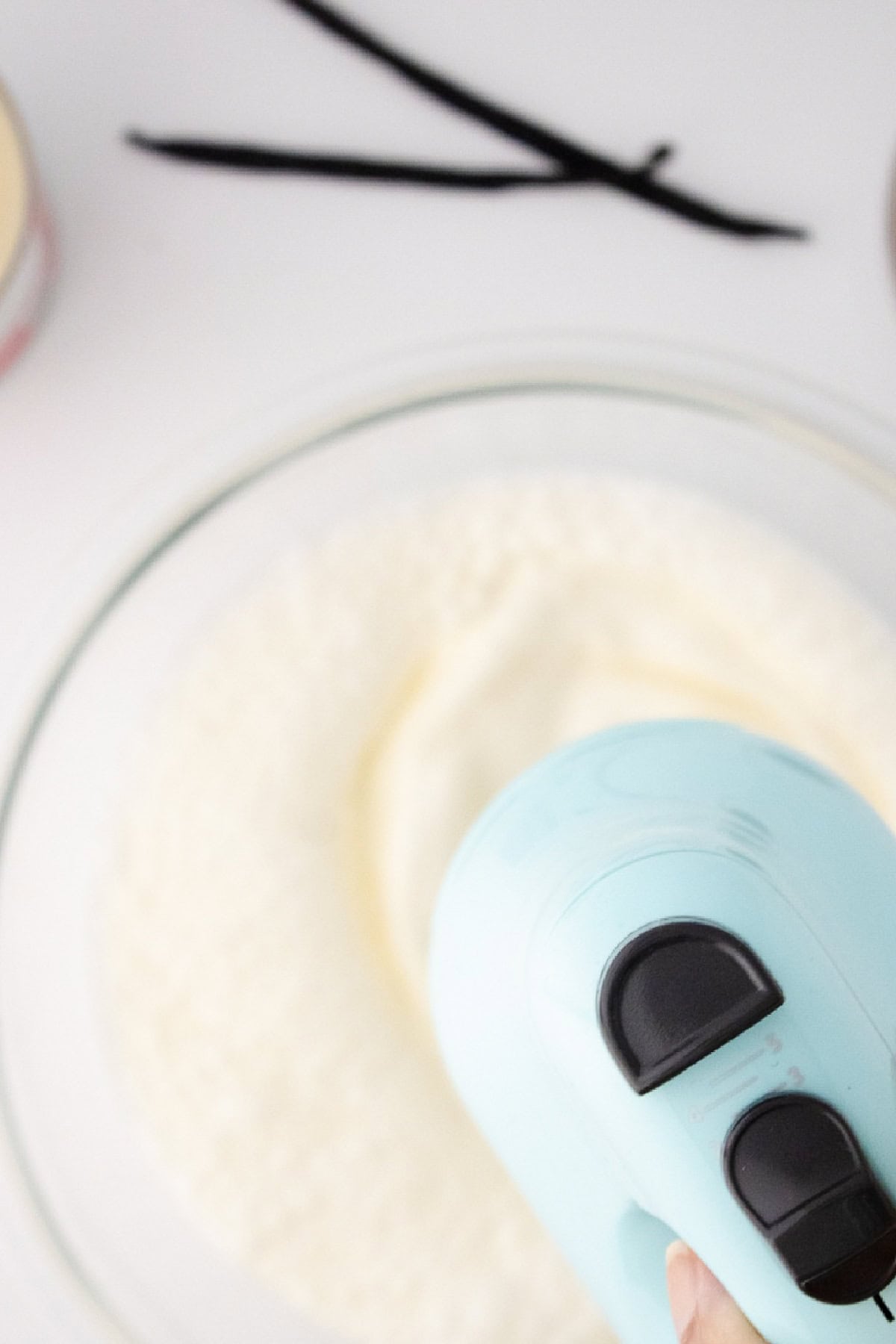 Whipping heavy cream with a hand mixer in a glass bowl to make homemade vanilla bean ice cream.