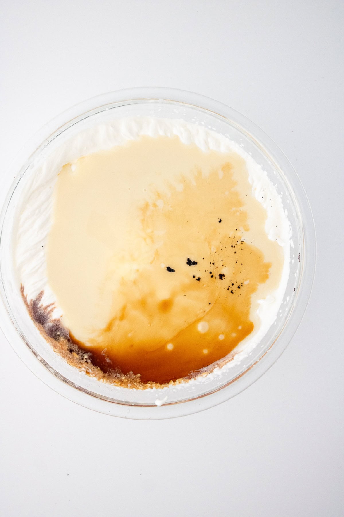 Adding sweetened condensed milk, vanilla extract, and scraped vanilla beans to whipped cream for vanilla ice cream mixture.