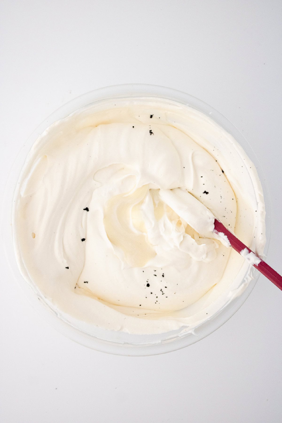 Folding vanilla bean mixture into whipped cream with a spatula to make creamy vanilla bean ice cream.