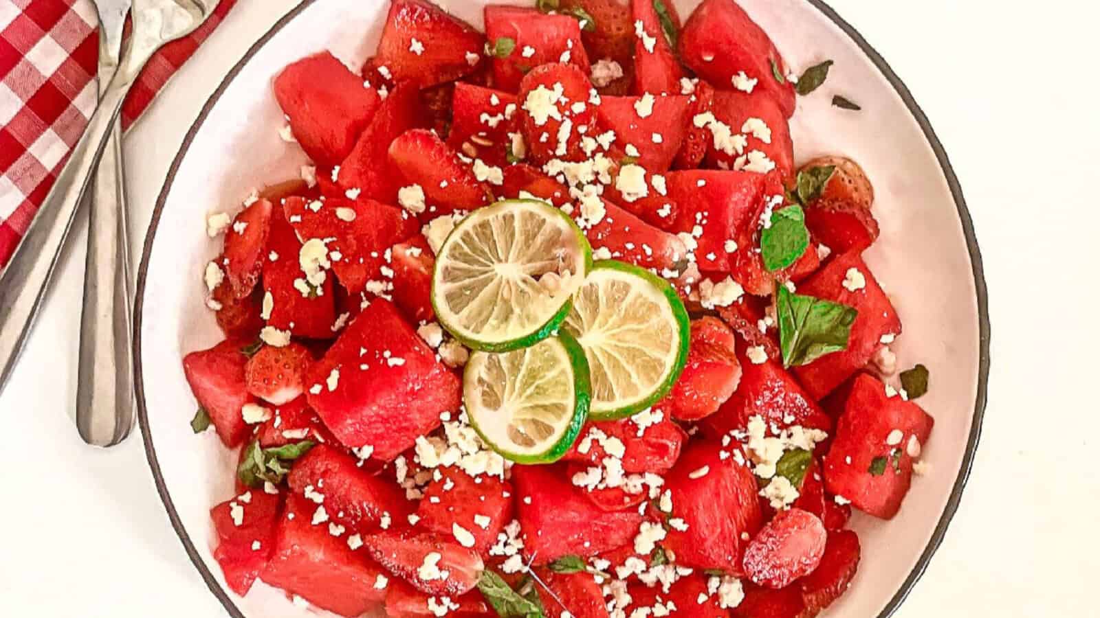 Top-down view of watermelon strawberry salad with feta, mint, and lime in a white bowl.