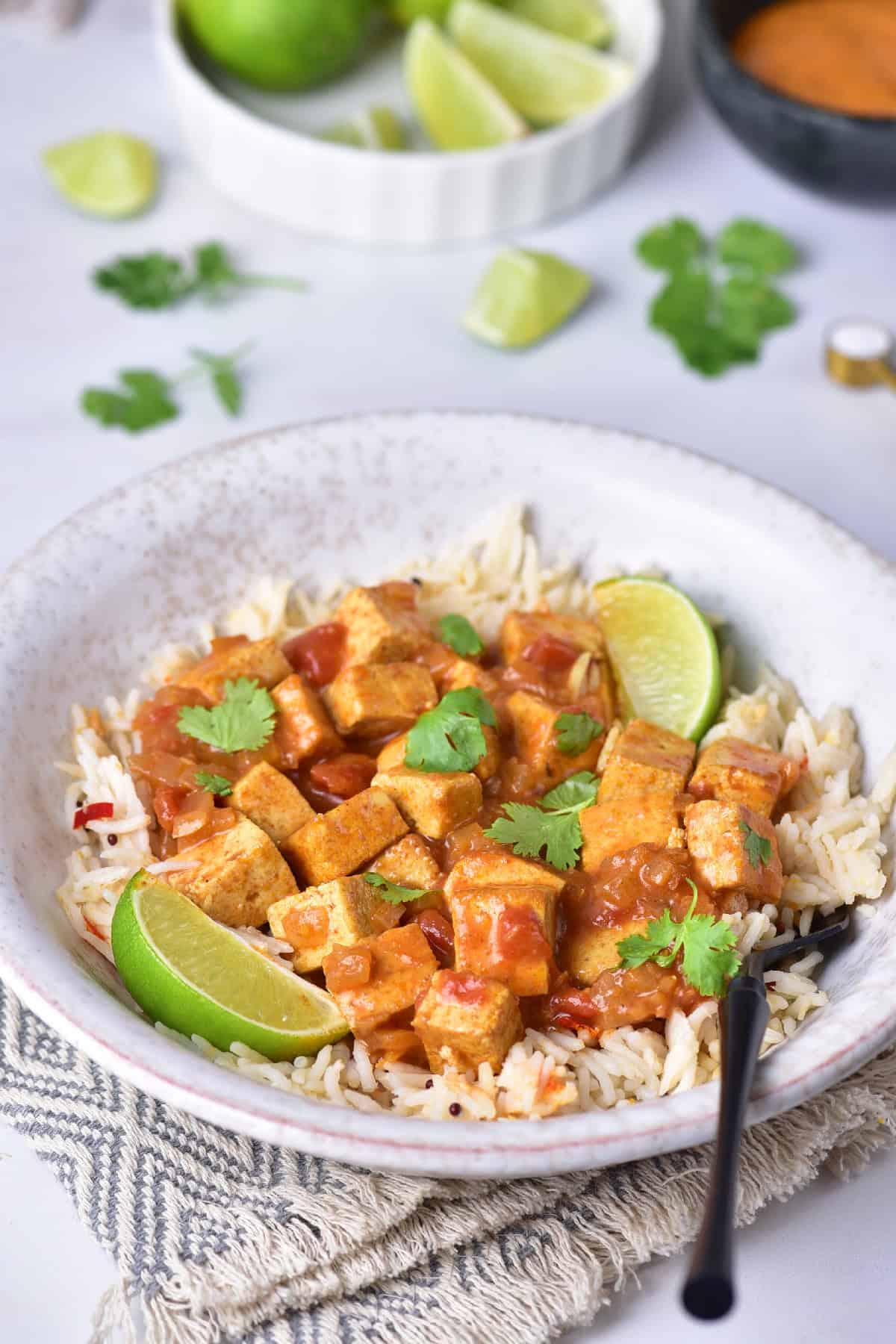 Close-up of yellow tofu curry served over fluffy rice, garnished with fresh cilantro and lime wedges in a rustic ceramic bowl.