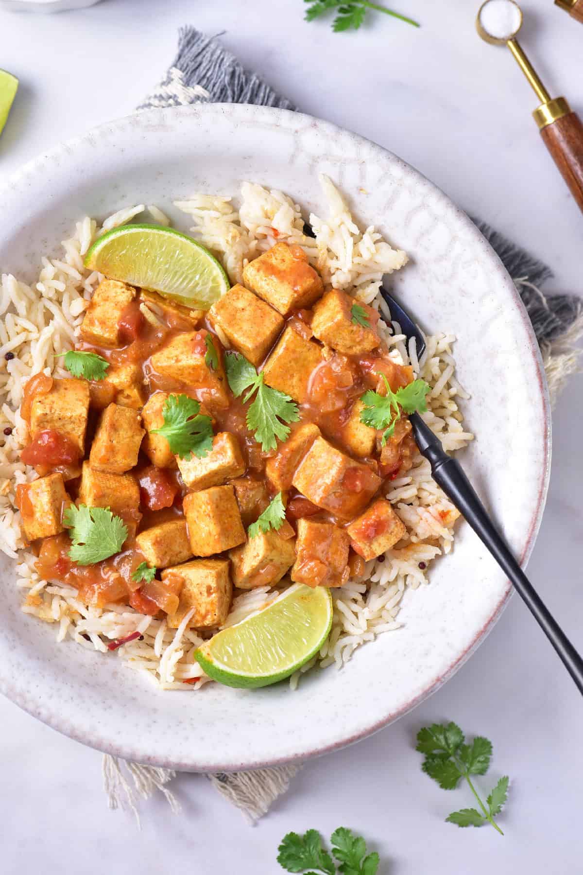 Flat lay of tofu curry with long-grain rice and lime, highlighting vibrant curry sauce and herbs in a minimalist setup.