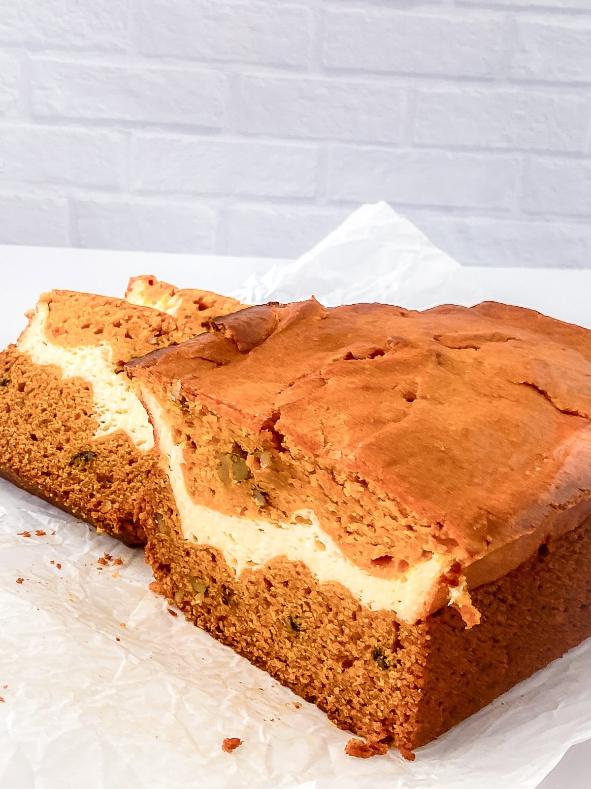 Whole loaf of cream cheese pumpkin bread on parchment paper with a creamy swirl visible inside after slicing.