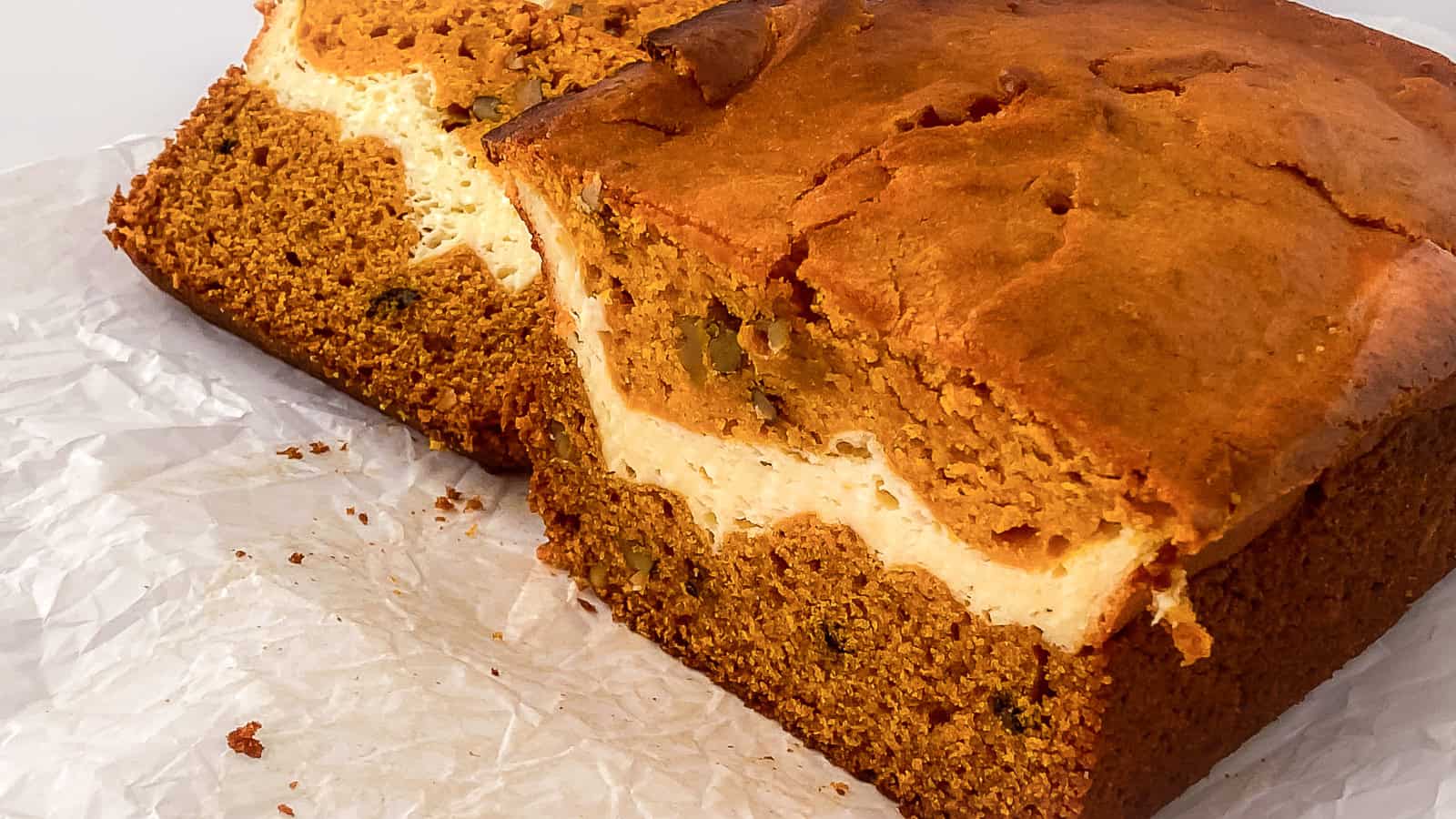 Close-up of moist cream cheese pumpkin bread slices showing a rich orange pumpkin layer swirled with creamy cheesecake filling and nuts.